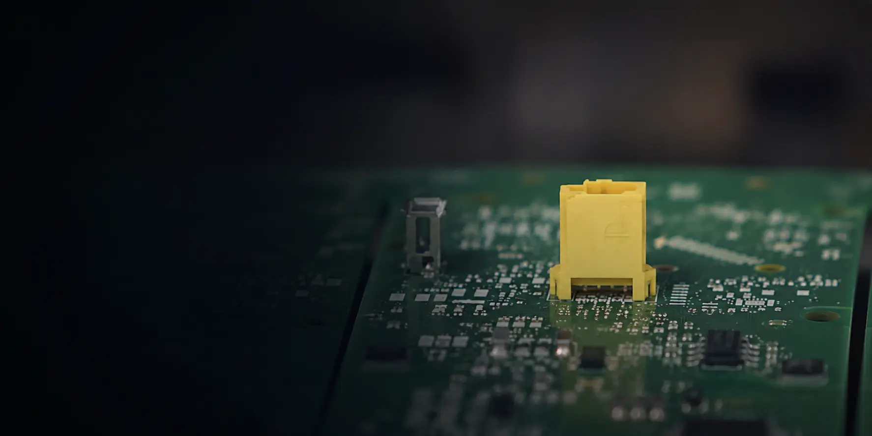 Close-up of a yellow connector mounted on a green circuit board during electronics assembly
