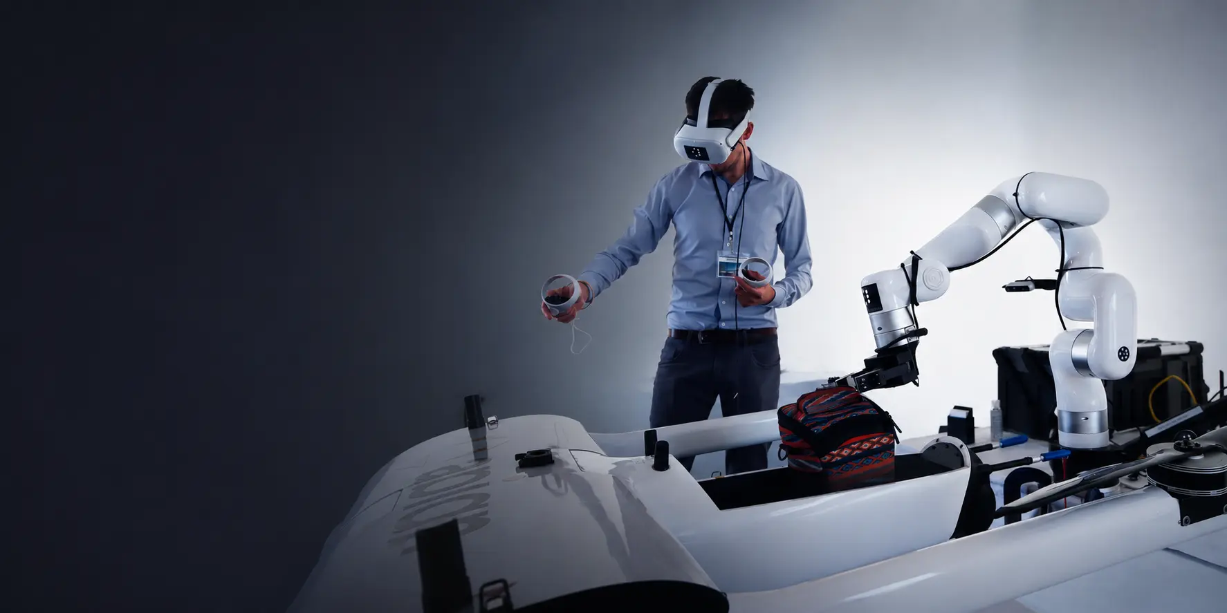 Operator in a VR headset using hand controllers to teleoperate a UFACTORY cobot over a workbench