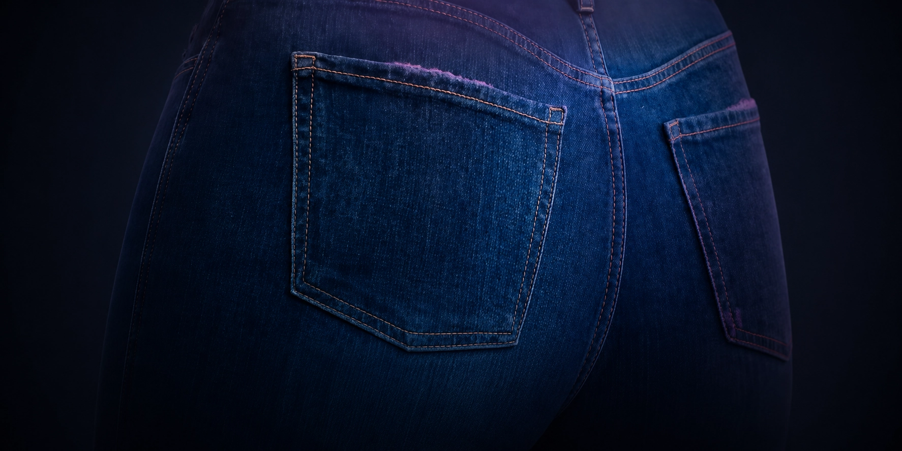 Close-up of denim jeans with pink-toned coating sprayed along the pocket edges