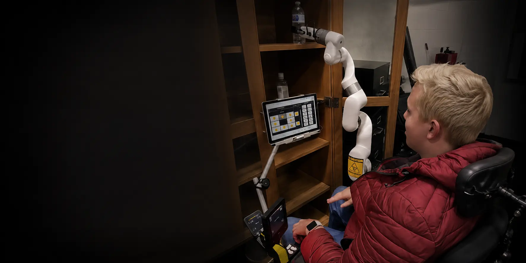 Wheelchair user selecting a task on a tablet interface as a UFACTORY xArm 6 retrieves a water bottle from a cabinet shelf