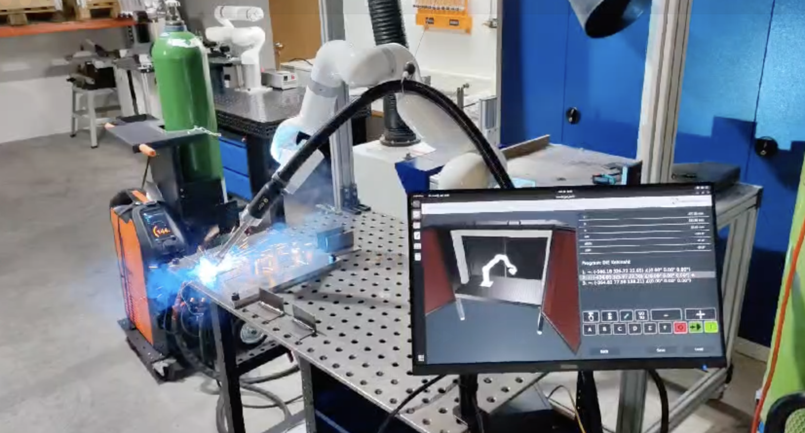 UFACTORY cobot welding a steel assembly on a fixture table, with gas cylinder, welding power source, and fume extraction in view